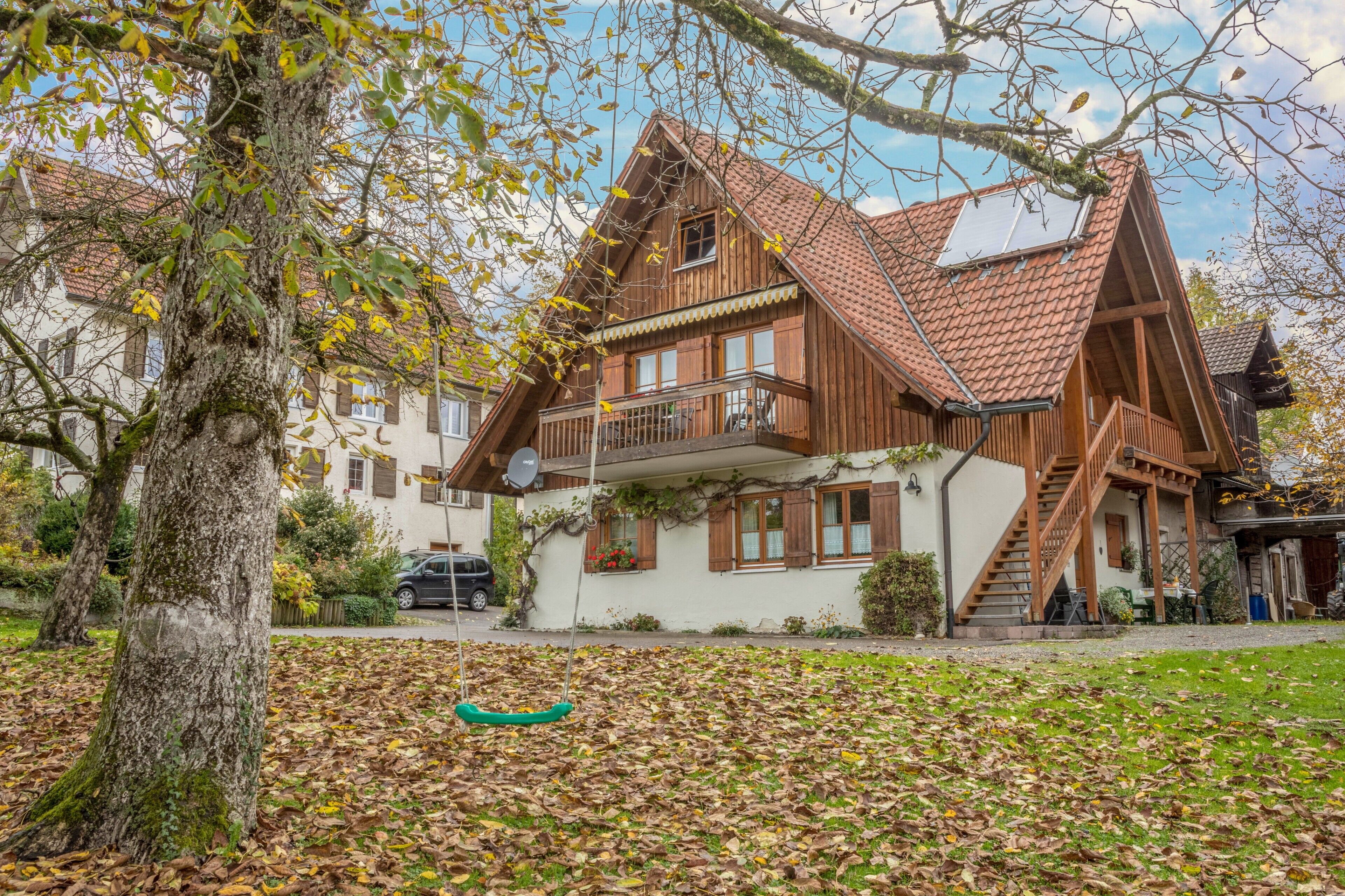 Ein traditionelles Holzhaus mit einem geneigten Dach, einem Balkon und einer Treppe, die zum Obergeschoss führt.