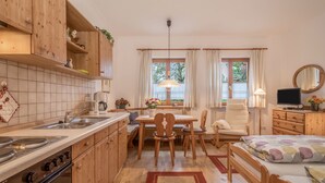 Una cocina compacta con armarios de madera, un comedor con mesa y sillas, una cama con colcha estampada y un televisor sobre un aparador.