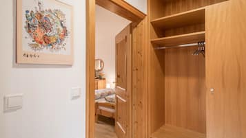 Ein Holzkleiderschrank mit Kleiderstange, ein Bett mit floraler Bettdecke und ein an der Wand befestigter Bilderrahmen.