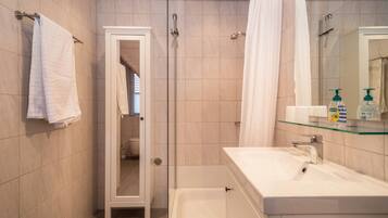 Ein Badezimmer mit Dusche, Waschbecken, einer Glasablage für Toilettenartikel und einem Handtuch, das an der Wand hängt.
