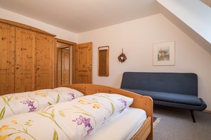 Une chambre à coucher avec un lit, une armoire en bois, un canapé bleu, un miroir et un tableau encadré accroché au mur.