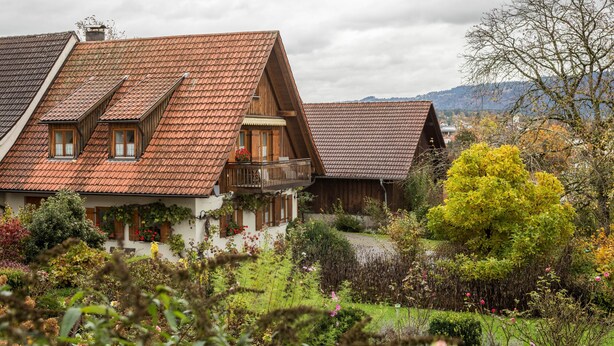 Un chalet tradicional con techo inclinado, un balcón y un jardín con diversas plantas y flores.