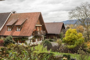 Un chalet traditionnel doté d’un toit en pente, d’un balcon et d’un jardin agrémenté de diverses plantes et fleurs.