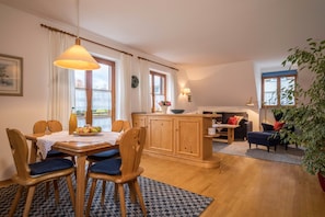 Un coin repas avec une table dressée pour quatre personnes, des chaises en bois, un tapis à motifs et un luminaire suspendu.