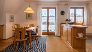 Un comedor con una mesa y sillas de madera, una lámpara colgante y vistas a través de un ventanal.