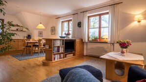 Una sala de estar acogedora con una mesa de comedor de madera, estanterías, un televisor y un ventanal con cortinas.
