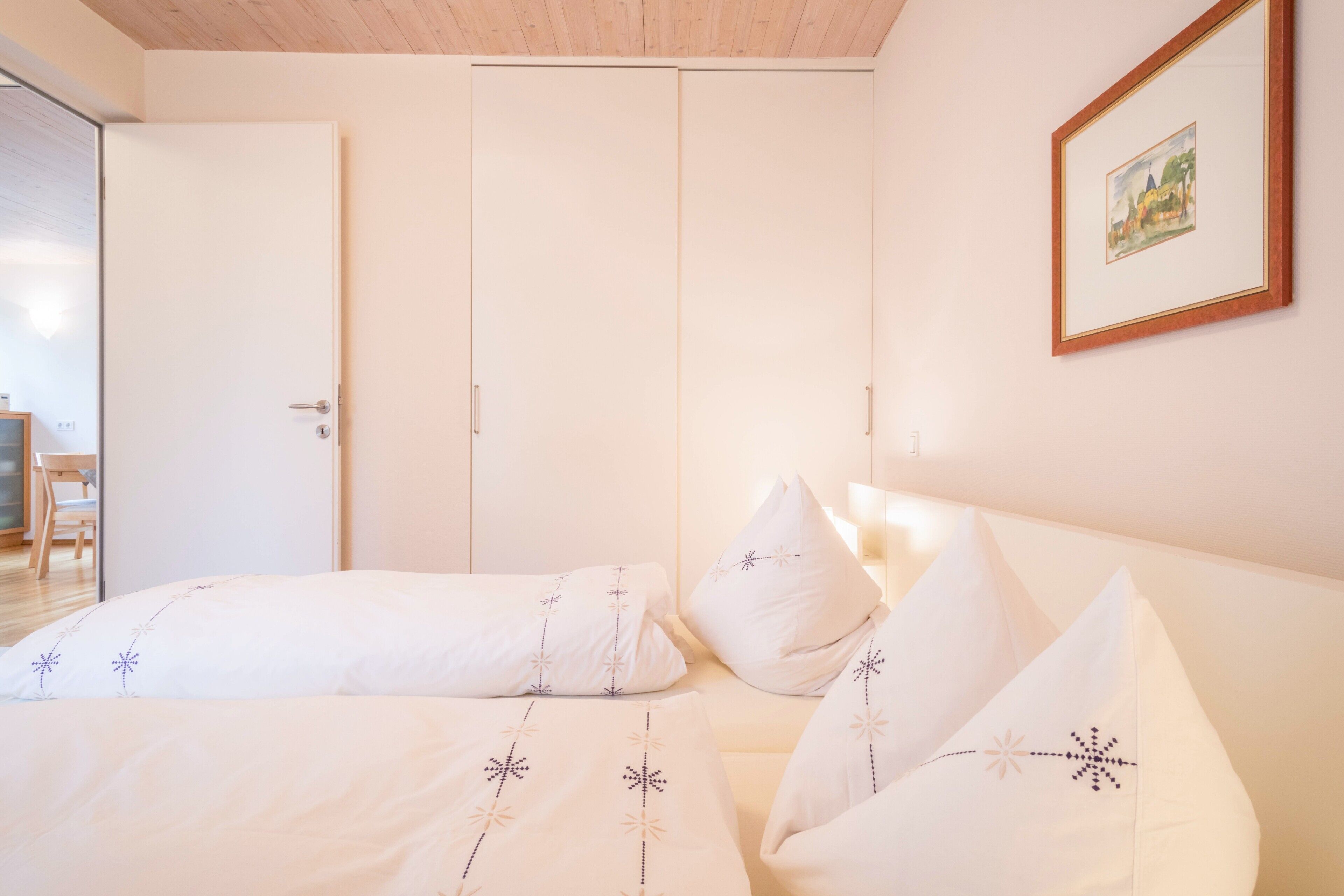 A bedroom with a bed, pillows, a door, and a framed picture on the wall.