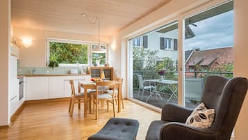Eine moderne Küche mit Holzschränken, ein Essbereich mit Tisch und Stühlen sowie eine große Schiebeglasdoor, die auf eine Terrasse im Freien führt.