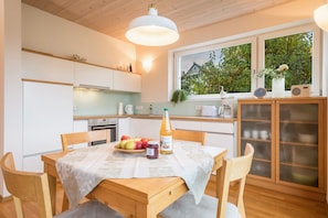 Una cocina moderna con una mesa de comedor preparada para dos personas, que incluye un frutero, una botella de jugo y un frasco de mermelada.