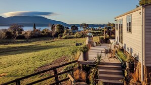 Une terrasse en bois menant à une maison offrant une vue sur un lac et des montagnes.