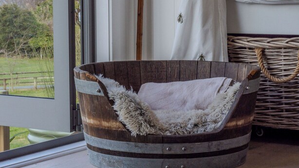 Une baignoire rustique en bois, une serviette blanche moelleuse, une canne en bois et un rideau blanc avec un manche en bois.