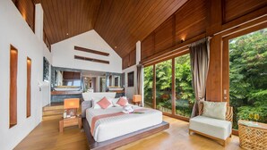 Un dormitorio amplio con una cama grande, una zona de estar y vistas a exuberante follaje.