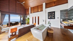 Una habitación de hotel moderna con una bañera grande, suelo de madera y un balcón con vistas al océano.