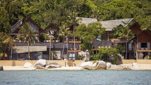 Un resort frente a la playa con varias cabañas de madera, rocas grandes y abundante vegetación.