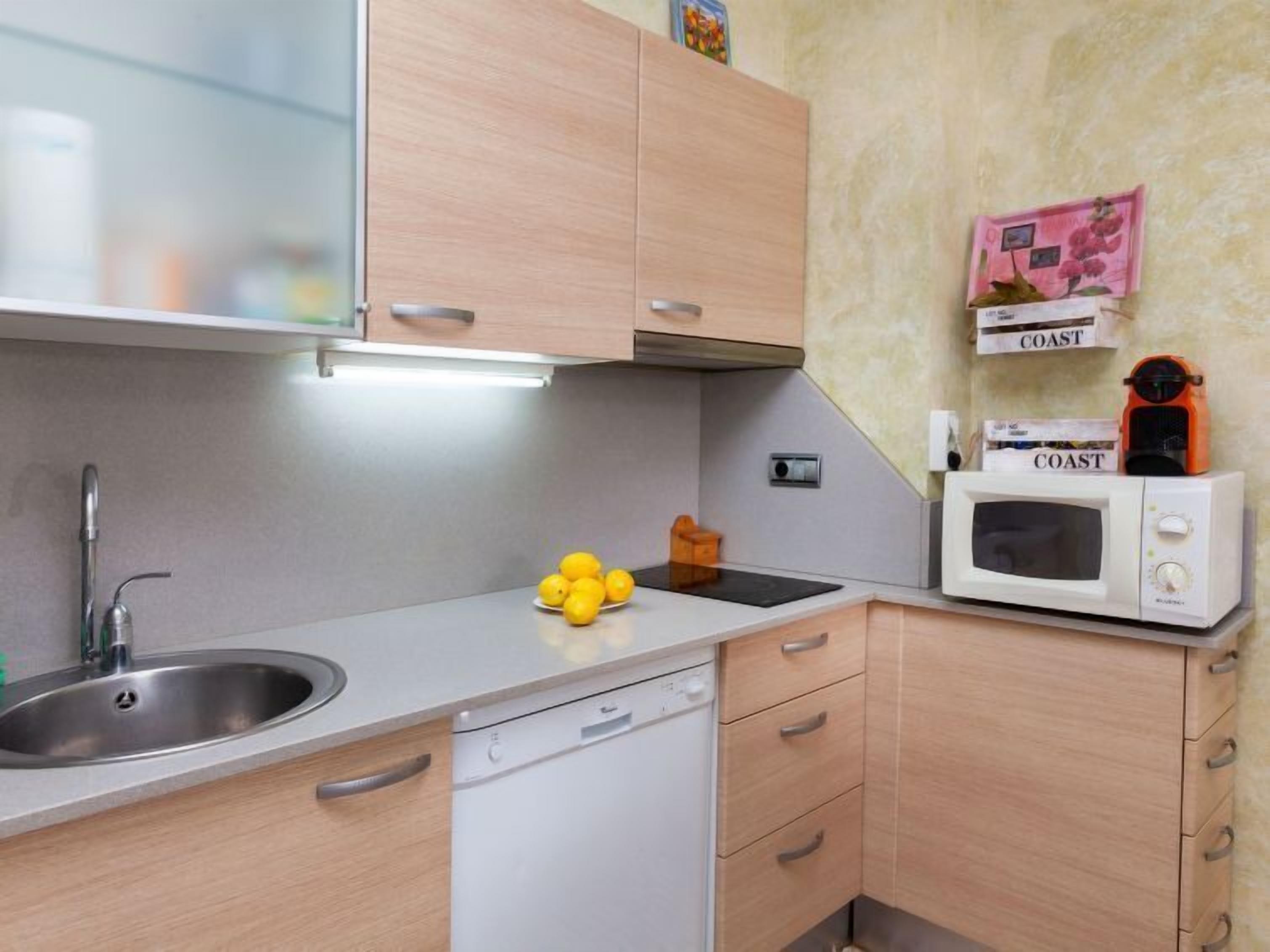 A compact kitchen with a sink, a microwave, and a small countertop with lemons.