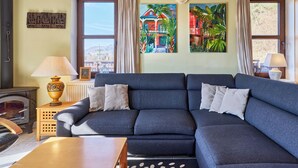 A living room with a dark blue sofa, a wooden table, a fireplace, and two windows with curtains. - Green Valley Park Stárkov 6 by Interhome (Stárkov)