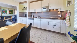 A modern kitchen with white cabinets, a microwave, and a dining area with a wooden table and chairs. - Green Valley Park Stárkov 6 by Interhome (Stárkov)