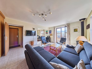 A living room with a sofa set, a television, a fireplace, and a dining area.