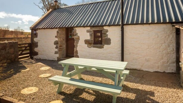 A rustic stone building with a metal roof, a wooden door, and a picnic table in front. - Sunflower Cottage by Interhome (Bridge of Marnoch)