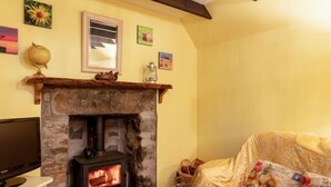 A cozy living room with a stone fireplace, a television, and a sofa with floral cushions. - Sunflower Cottage by Interhome (Bridge of Marnoch)