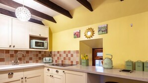 A kitchen with white cabinets, a microwave, a toaster, and a kettle. There are two stools and a window with a view of the outside. - Sunflower Cottage by Interhome (Bridge of Marnoch)
