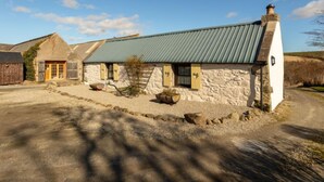 A stone building with a metal roof, a wooden door, and a gravel driveway. - Sunflower Cottage by Interhome (Bridge of Marnoch)