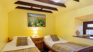 A room with two single beds, wooden headboards, a nightstand with a lamp, a painting of sunflowers, and a window with a view. - Sunflower Cottage by Interhome (Bridge of Marnoch)