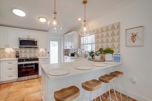 A modern kitchen with white cabinetry, a built-in oven, a microwave, and a large island with stools.