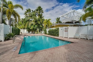 A swimming pool with a white deck, surrounded by palm trees and a white gazebo.