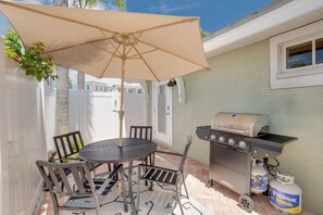 Een terras buiten met een ronde tafel, stoelen, een barbecue en propaanflessen.