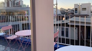 A balcony with pink chairs and a table, overlooking a cityscape with buildings and a clear sky. - Just Mansion (Seoul)