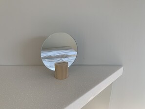 A round mirror on a white shelf with a small wooden object in front of it.