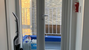 A narrow hallway with a sliding glass door leading to a balcony. A vacuum cleaner is placed against the wall on the left. - Just Mansion (Seoul)