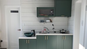 A kitchen with a white tiled backsplash, green cabinets, a black sink, and a built-in microwave. - Just Mansion (Seoul)