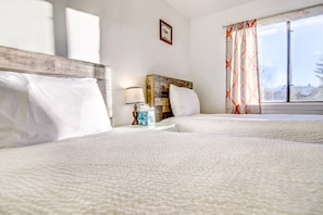Une chambre d’hôtel avec deux lits, une table de chevet avec une lampe et des mouchoirs, un tableau encadré au mur et une fenêtre avec des rideaux.