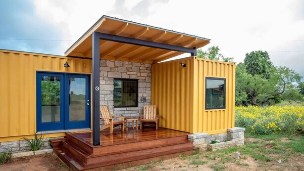 A modern house with a yellow exterior, a stone facade, and a wooden deck with chairs. - Groovy!!! at Odonata Escape -- retro chic container room in the country (Fredericksburg)