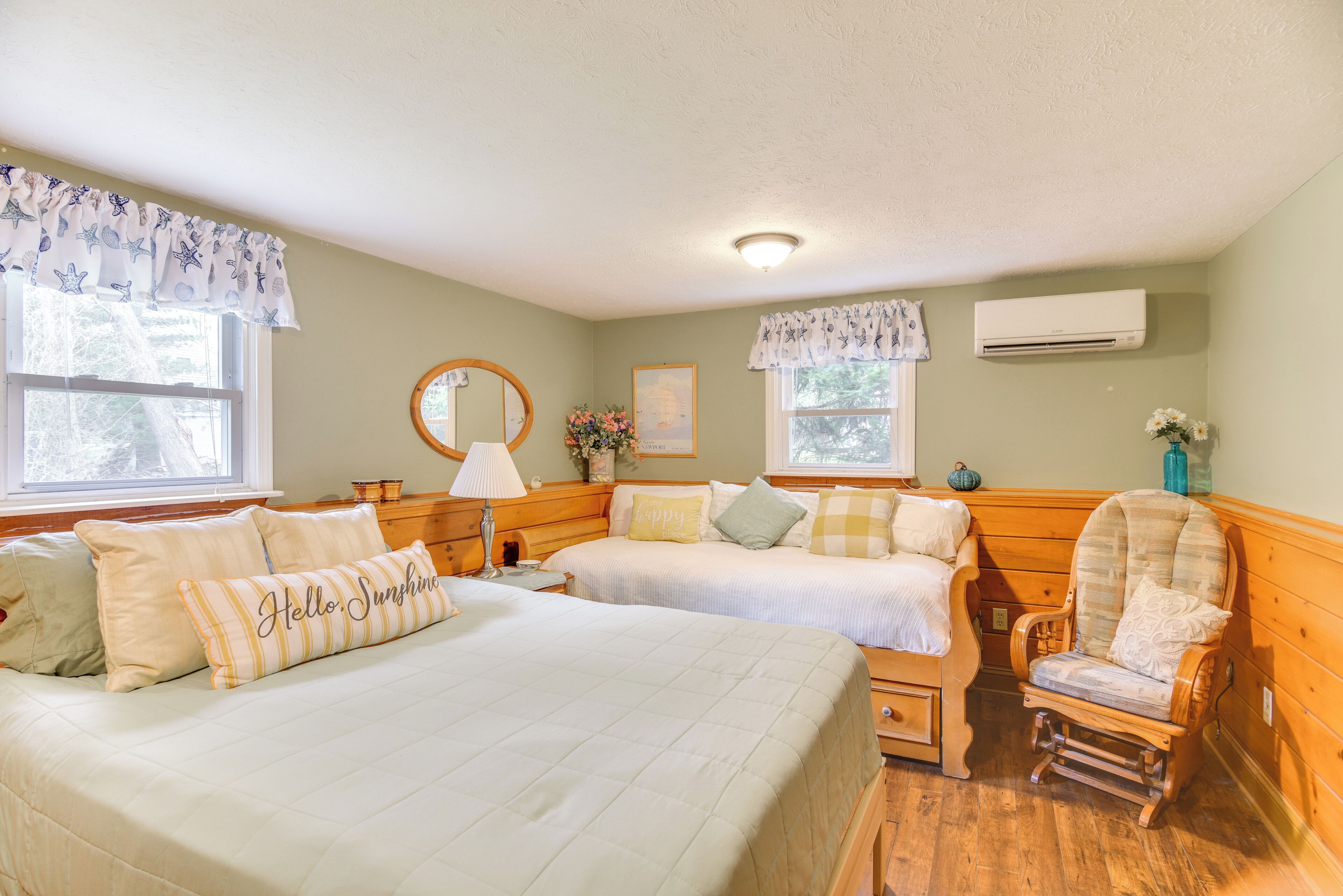A room with two beds, a rocking chair, a mirror, and an air conditioning unit.