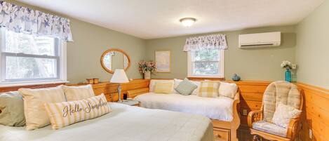 A room with two beds, a rocking chair, a mirror, and an air conditioning unit.