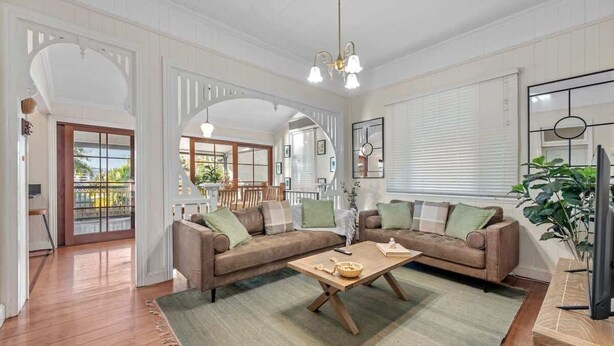 A spacious living room with a large sofa set, a wooden coffee table, and a television. - Comfy Character QLD’r ~ 3Bed House w/Parking (Woolloongabba)
