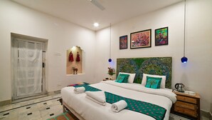 Une chambre d’hôtel avec un grand lit, un ventilateur de plafond, une table de chevet avec une machine à café et un mur orné de trois œuvres d’art encadrées.