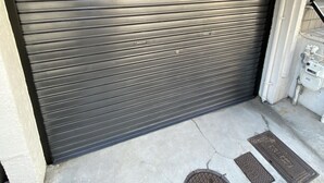 A closed garage door with a metal vent and a manhole cover on the ground. - Kyo Yado Inari (Kyoto)