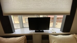 A hotel room with a TV on a stand, a window with blinds, and two white pillows on the bed. - Kyo Yado Inari (Kyoto)