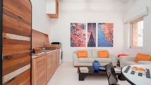 A modern living room with a wooden cabinet, a sofa with orange cushions, a coffee table with a vase, and abstract paintings on the wall. - The Waterview Alcove (Venice)