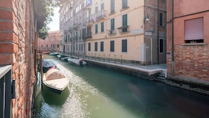 A narrow canal with boats docked along the sides, flanked by multi-story buildings with balconies and windows. - The Waterview Alcove (Venice)
