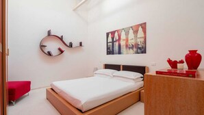 A bedroom with a bed, a red vase, a bookshelf, and a painting on the wall. - The Waterview Alcove (Venice)