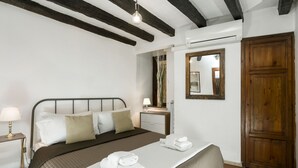Ein ordentlich bezogenes Bett mit braunem Kopfteil, ein Nachttisch mit Lampe, ein Holzschrank und ein Spiegel an der Wand.