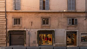 A building with multiple windows, some with shutters, and a ground-floor shop with mannequins displaying clothing.