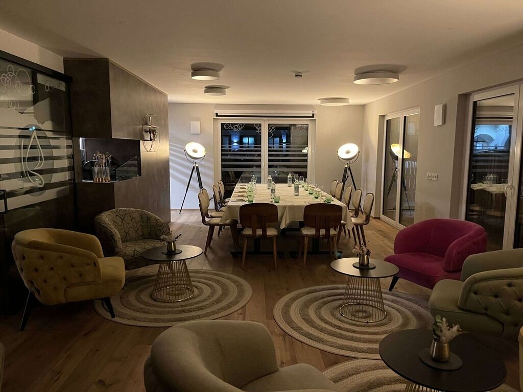Ein modernes Wohnzimmer mit Essbereich, ausgestattet mit einem langen Tisch für sechs Personen, umgeben von Sofas und Sesseln, mit einem großen Fenster, das natürliches Licht hereinlässt.