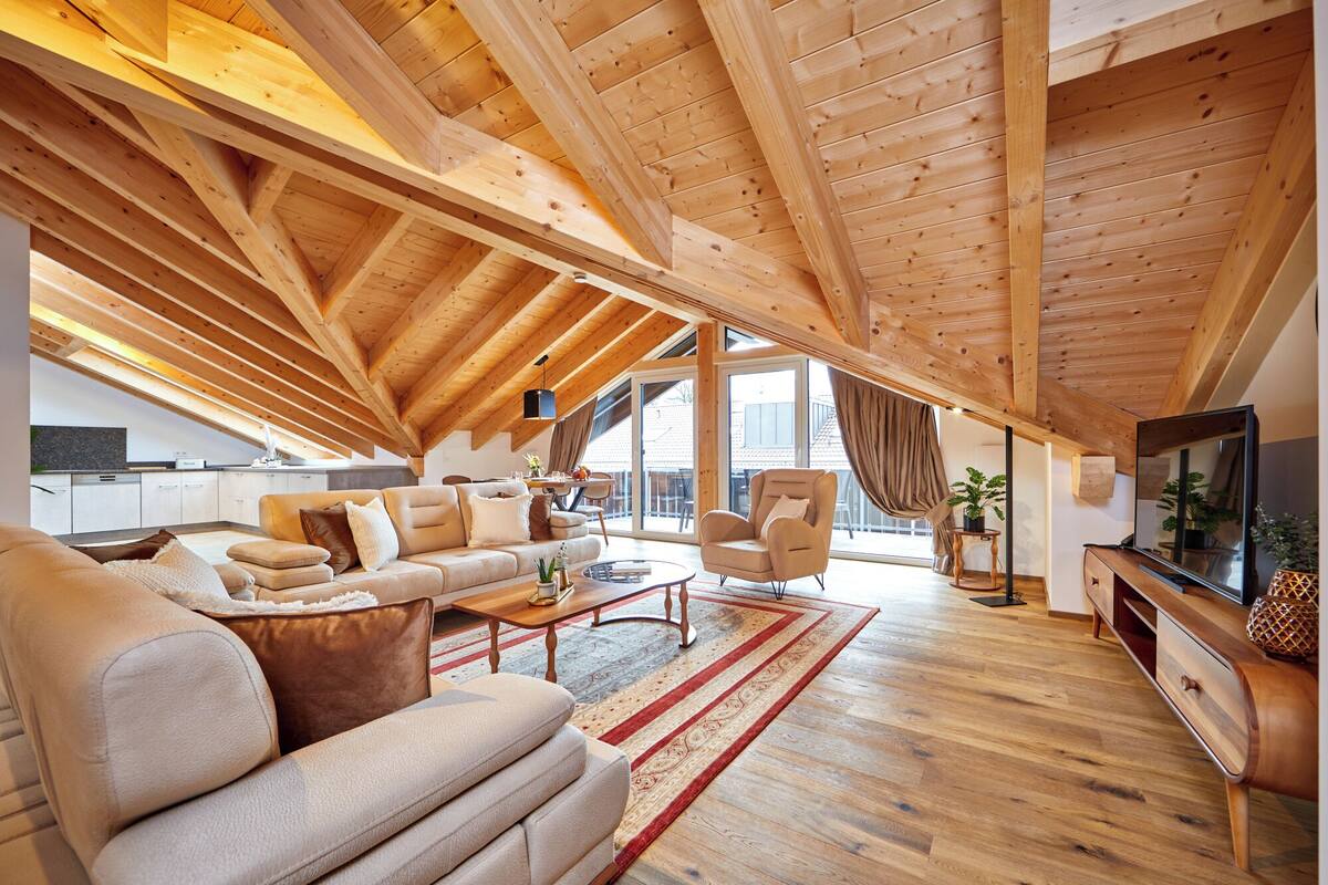 An attic room with a wooden ceiling, a sofa, a TV, and a dining area.