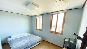 A bedroom with a bed, two windows, a ceiling fan, and a wooden desk with a computer. - Sanbangsan Parktel - Hostel (Seogwipo)
